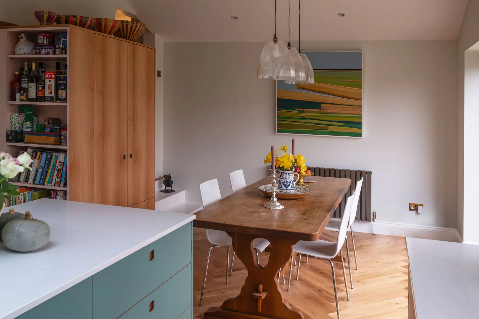A kitchen in Greenwich, London, with Blue Green cabinetry by Pluck, white worktops, parquet flooring and art from around the world.