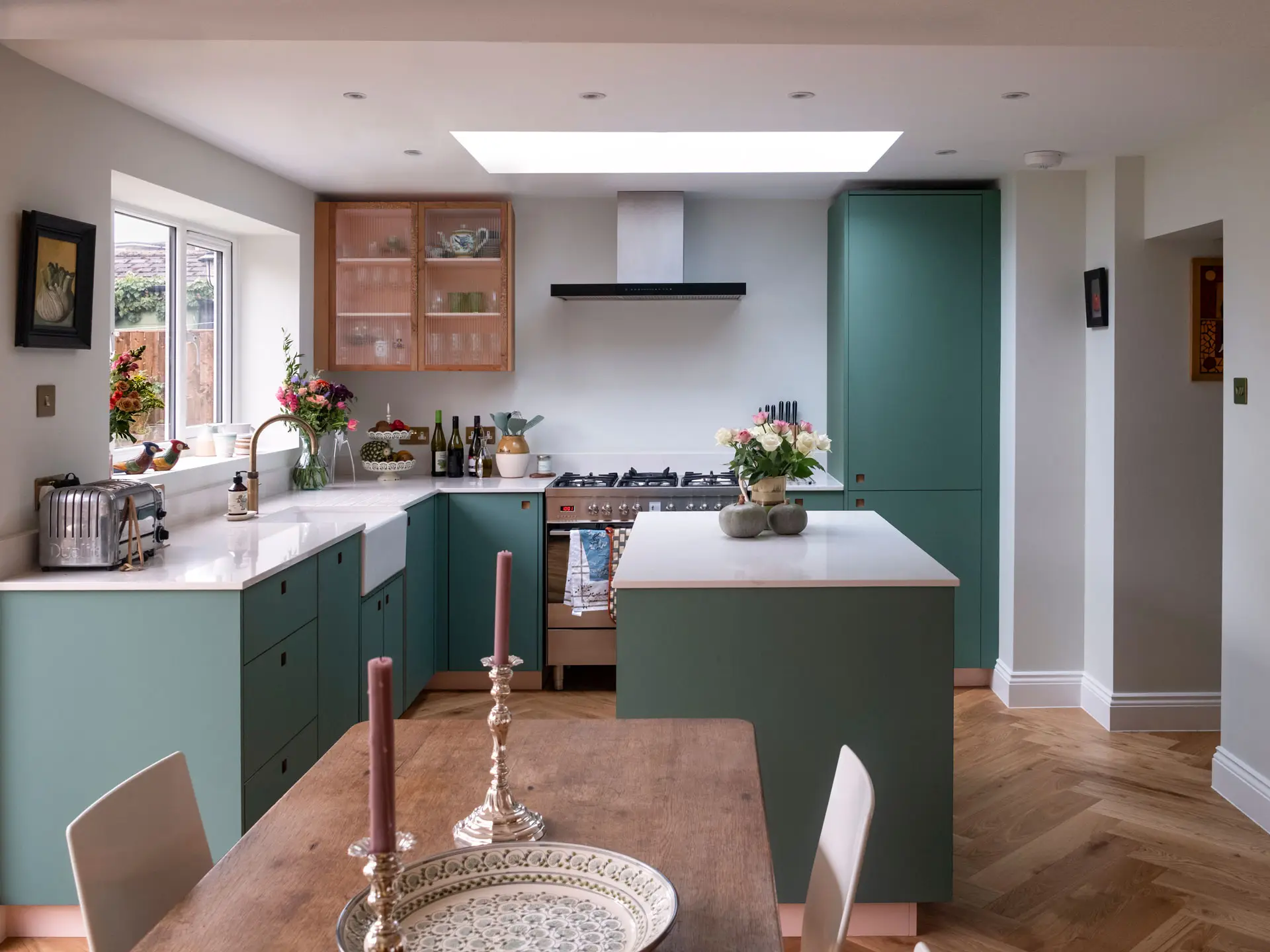 A kitchen in Greenwich, London, with Blue Green cabinetry by Pluck, white worktops, parquet flooring and art from around the world.