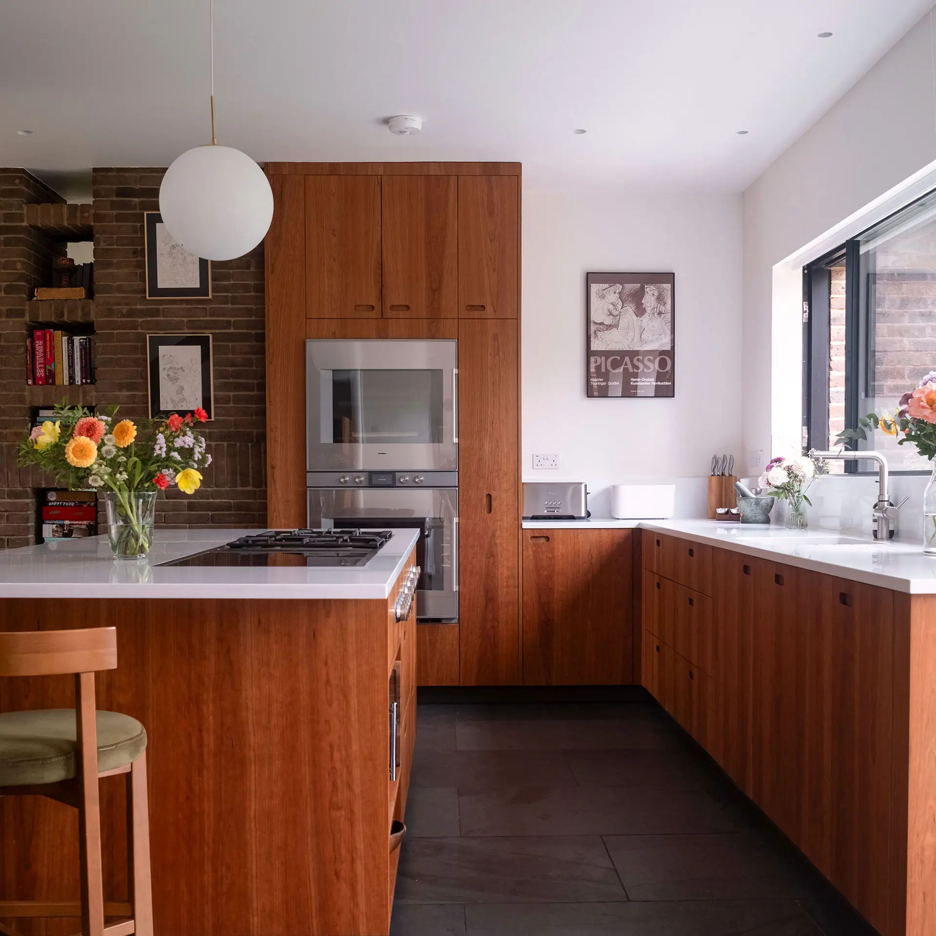 A minimalist Kitchen with stainless steel worktops, a single wooden shelf on the wall and Cherry cabinetry.