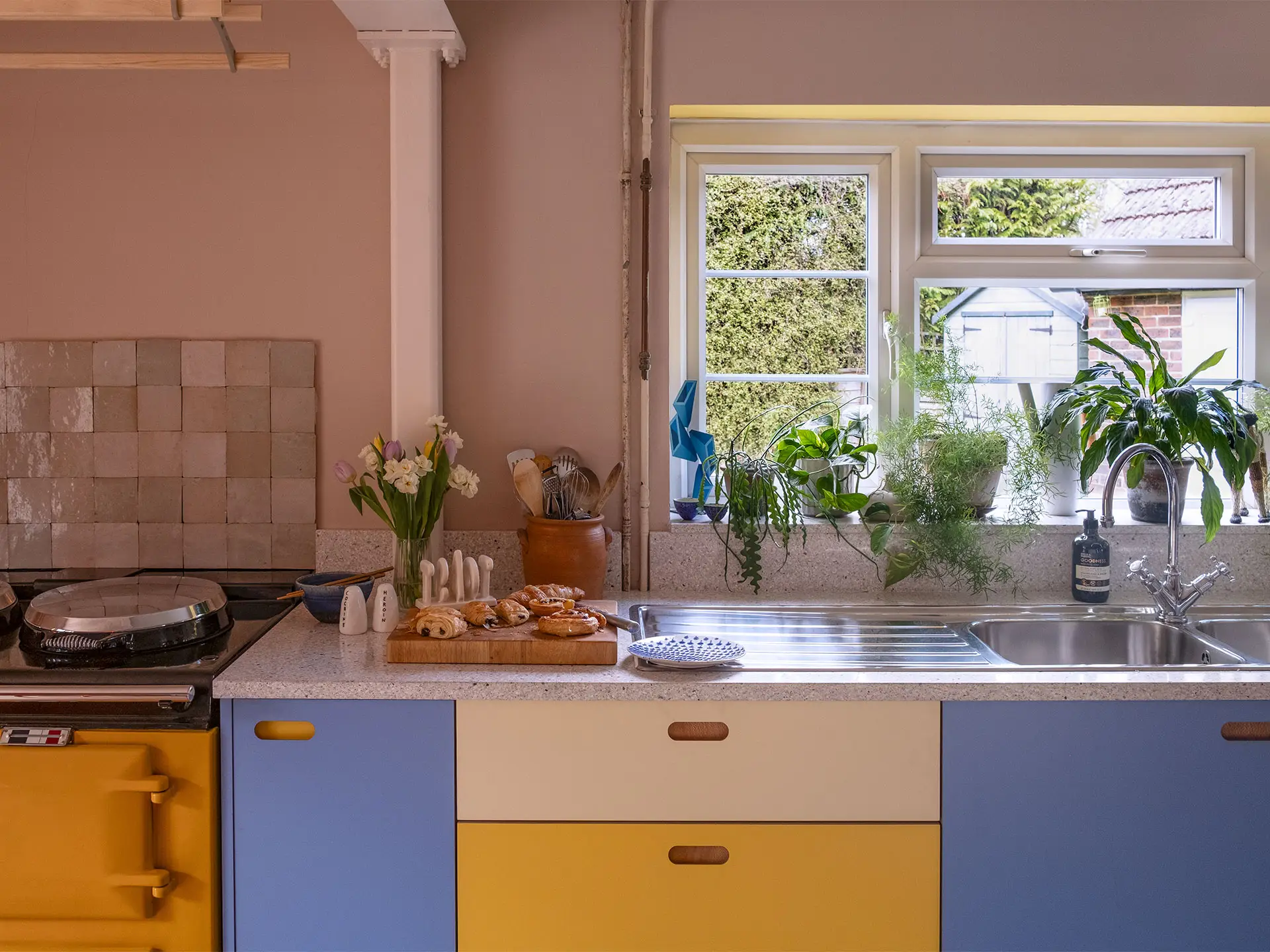 A colourful countryside kitchen with a bright yellow AGA and Pluck cabinetry, including an island.