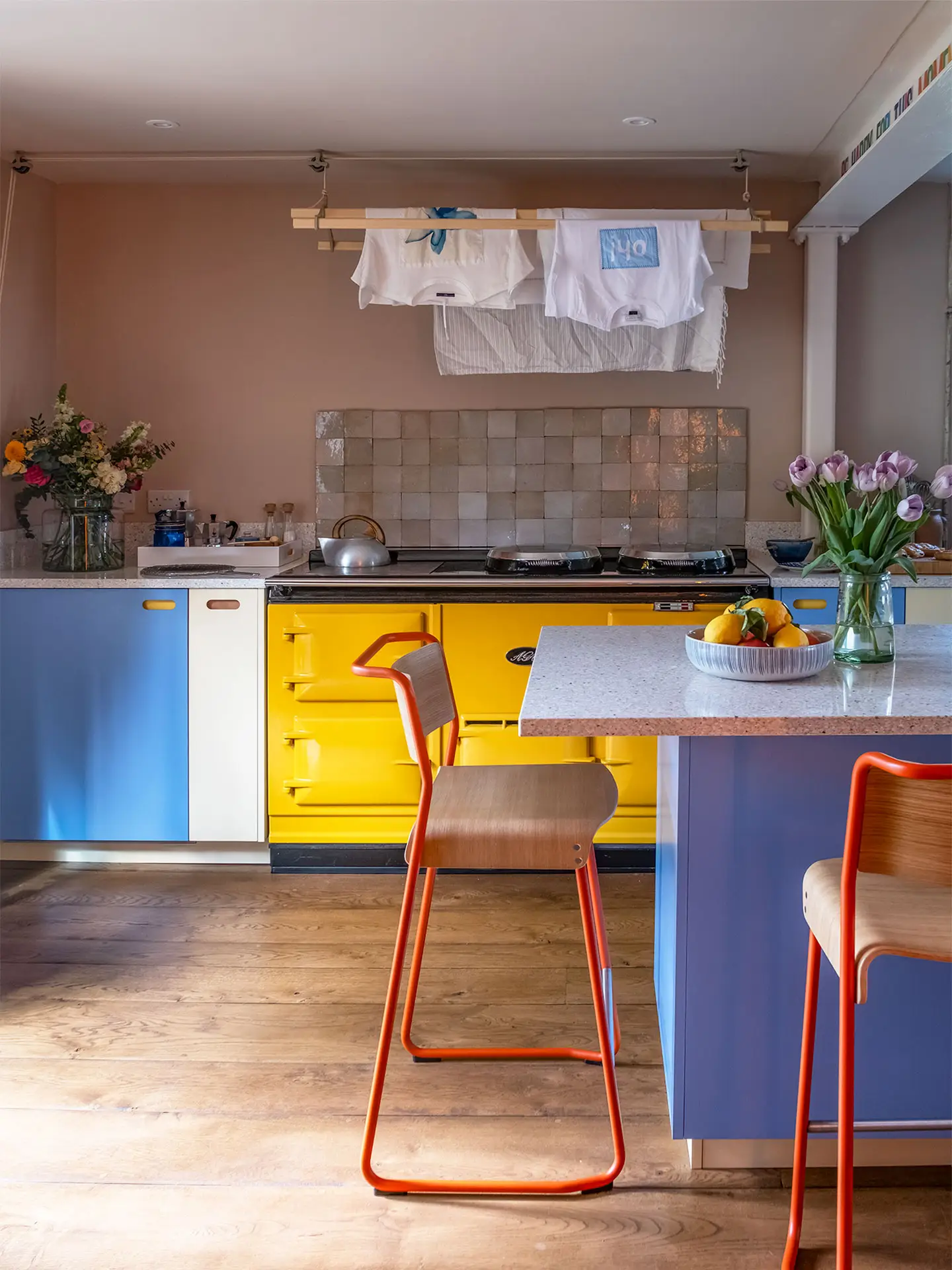 A colourful countryside kitchen with a bright yellow AGA and Pluck cabinetry, including an island.