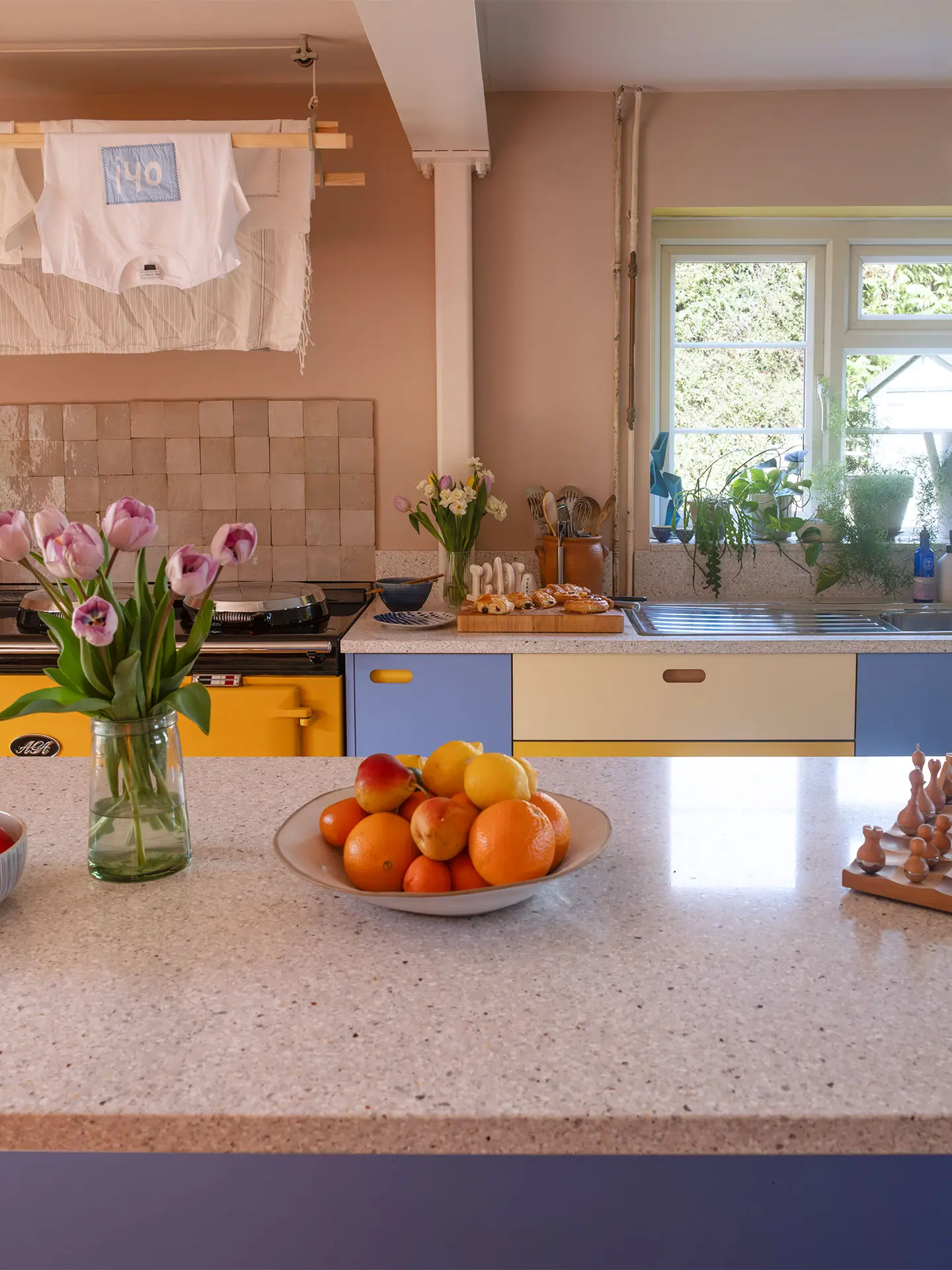 A colourful countryside kitchen with a bright yellow AGA and Pluck cabinetry, including an island.