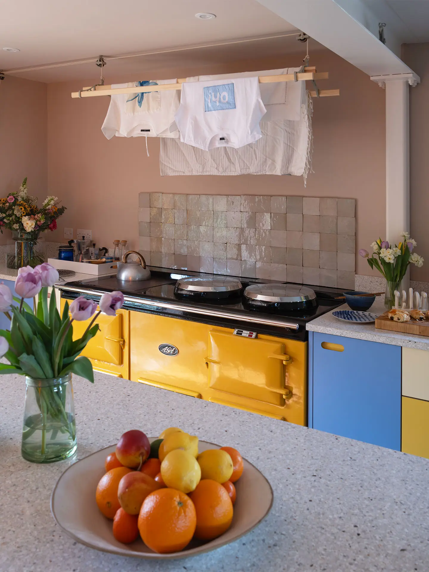 A colourful countryside kitchen with a bright yellow AGA and Pluck cabinetry, including an island.