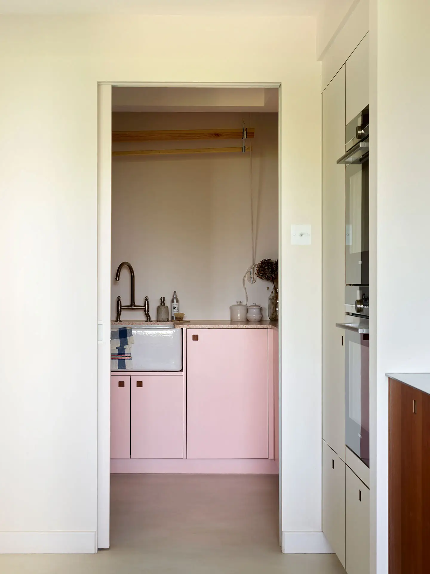 White, cherry wood and pink cupboards in a london kitchen by Pluck, with an island and dining area.