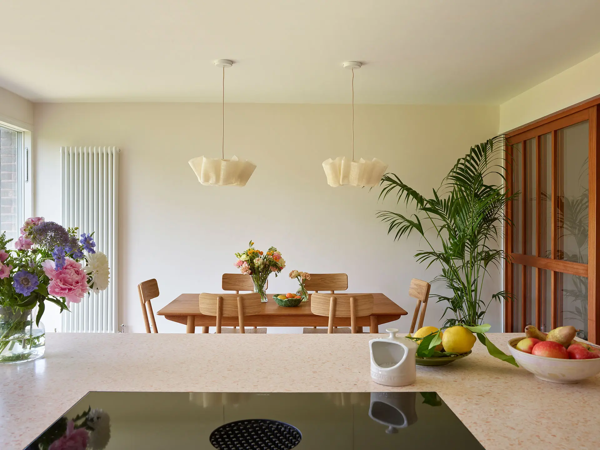 White, cherry wood and pink cupboards in a london kitchen by Pluck, with an island and dining area.
