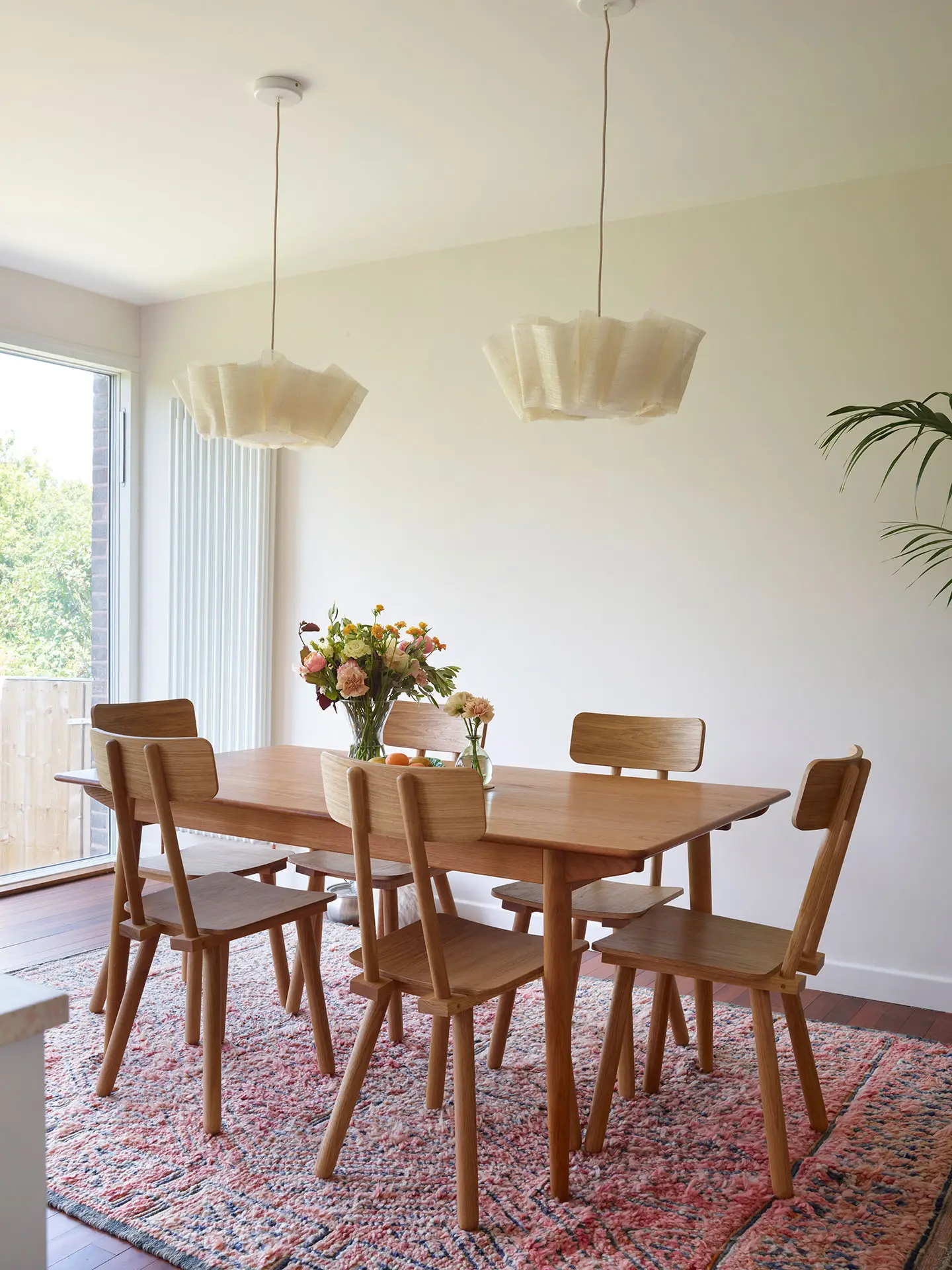White, cherry wood and pink cupboards in a london kitchen by Pluck, with an island and dining area.