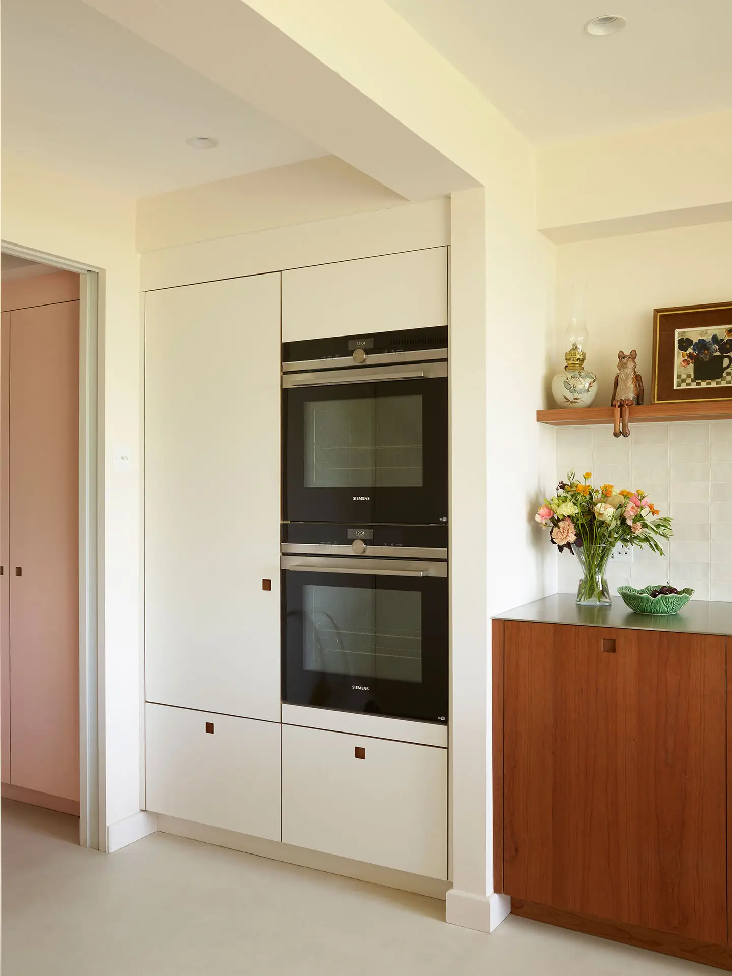 A Pluck kitchen in London with white and cherry wood custom cabinetry and a soft pink utility.